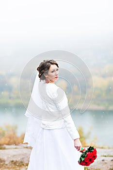 Young attractive bride with the bouquet of red roses over snowy Christmas background