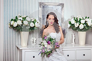 Young attractive bride with flowers indoors . Bride`s morning. Happy Bride waiting groom.
