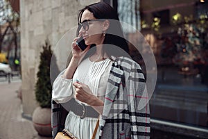 Young attractive brunette female in sunglasses talking on mobile phone at street.