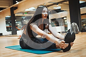 Young attractive brunette girl enlacing her sport shoes after practicing workout and crossfit training on blue yoga mat.