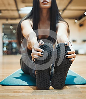 Young attractive brunette girl enlacing her sport shoes after practicing workout and crossfit training on blue yoga mat.