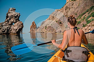 A young attractive brunette in a swimsuit swims on a kayak around volcanic rocks, like in Iceland. Back view. Travel