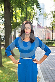 Young attractive brunette woman in blue dress pouting emotions of resentment in a park in the city