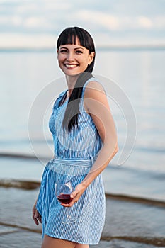 A young attractive brunette woman, in a blue dress, walks along the seashore. Portrait of a smiling woman on vacation