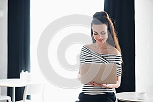Young attractive brunette woman holding a laptop and typing, while looking at the screen. Adult female surfing the