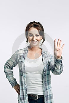 Young attractive brunette woman in a plaid shirt and white t-shirt shows: give five with your left hand.