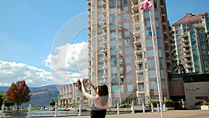 Young attractive brunette woman in a plaza in downtown Kelowna taking photos of a fountain. HD 24PS.