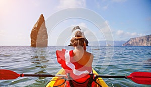 Young attractive brunette woman in red swimsuit, talk by phone while swimming on kayak around volcanic rocks, like in