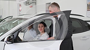 Young attractive brunette woman sits behind the wheel of a new car in a car showroom