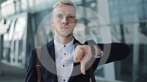 Young attractive business man standing near airport and looking into the camera. Man shows thumb up and down