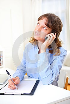 Young attractive business woman copying data on paper while phoning