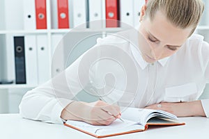 Young attractive business woman making notes at office workplace.