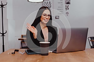 Young attractive business woman waving greeting at video conference on laptop online meeting