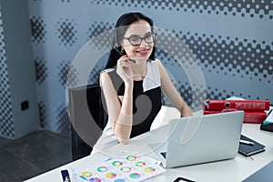 Young attractive businesslady in black dress and glasses sit at