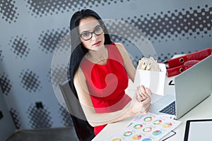 Young attractive businesslady in red dress and glasses sit at th