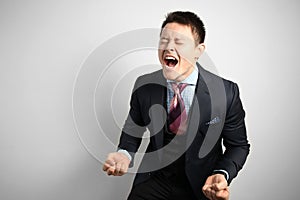 Young attractive businessman businessman in suit on gray background in rage, anger and madness