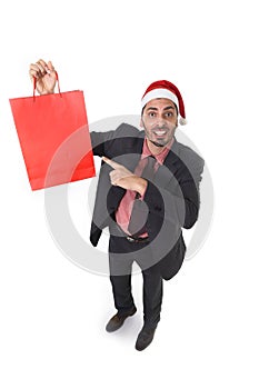 Young attractive businessman in Christmas Santa hat holding and pointing red shopping bag in December and New year sale