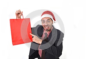 Young attractive businessman in Christmas Santa hat holding and pointing red shopping bag in December and New year sale