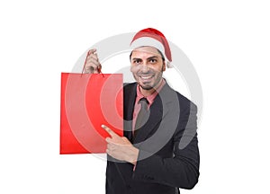 Young attractive businessman in Christmas Santa hat holding and pointing red shopping bag in December and New year sale