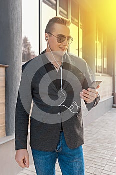 A young attractive businessman of European appearance in a jacket and shirt style, wears sunglasses and listens to music in