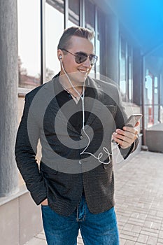 A young attractive businessman of European appearance in a jacket and shirt style, wears sunglasses and listens to music in