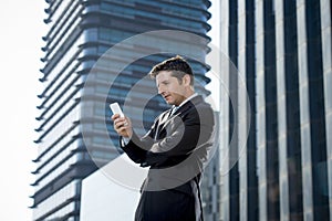 Young attractive businessman in suit and necktie looking text message at mobile phone outdoors