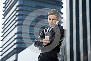 Young attractive businessman in suit and necktie looking text message at mobile phone outdoors