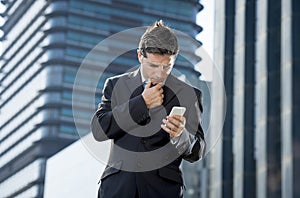 Young attractive businessman in suit and necktie looking text message at mobile phone outdoors
