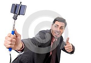 Young attractive businessman in suit and tie taking selfie photo with mobile phone camera and stick posing happy