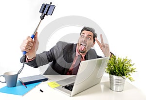 Young attractive businessman in suit and tie taking selfie photo with mobile phone camera and stick posing happy