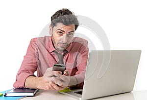 Young attractive businessman working at office desk with mobile phone and computer laptop looking bored and tired