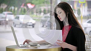 Young attractive businesswoman sitting in a coffee shop doing her job. she holds documents in her hands and looks in notebook