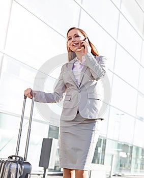 Young attractive businesswoman talking on smartphone while walking with her suitcase in airport