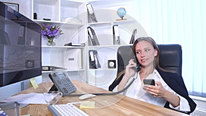 Young attractive businesswoman talking on telephone and using smartphone in the office and smiling