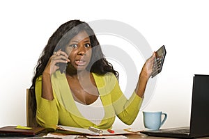 Young attractive and busy black afro American business woman working at home office computer desk talking on the phone holding cal