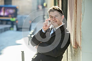 Young attractive and busy businessman with blue eyes wearing suit and tie talking business on mobile phone outdoors