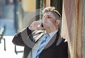 Young attractive and busy businessman with blue eyes wearing suit and tie talking business on mobile phone outdoors