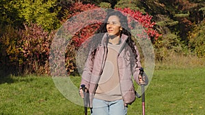 Young attractive carefree woman hiker travels with backpack trekking sticks walking outdoors in autumn park admiring