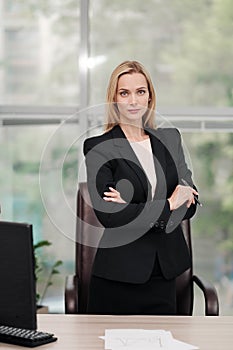 Young attractive Caucasian blond woman in black business suit sits at desk in bright office. Studying paper documents