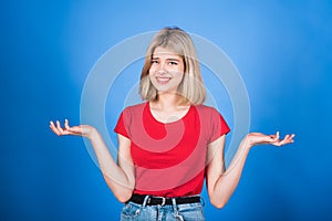 Young and attractive caucasian blonde girl in casual clothes is confused and smirking, shrugging her shoulders.