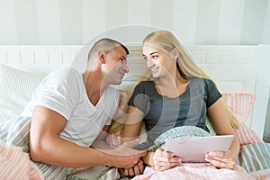 Young attractive caucasian couple in bed. Woman holding digital tablet, man lovingly looking at her, hoping to catch her attention photo