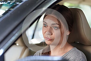 Young attractive caucasian woman behind the wheel driving a car with grimace of disappointment, frustration or displease.