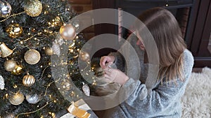 Young attractive caucasian woman decorates Christmas tree by gold balls, christmas eve, x-mas arrangements, garlands and