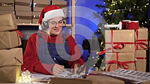 Young attractive caucasian woman dressed as santa claus takes an order online using headset and smart phone prepares