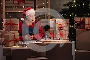 Young attractive caucasian woman dressed as santa claus takes an order online using headset and smart phone prepares