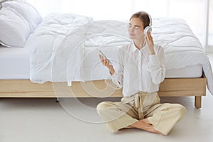 Young attractive caucasian woman wearing white casual clothes with headphone. She listening music or radio by using cell phone or