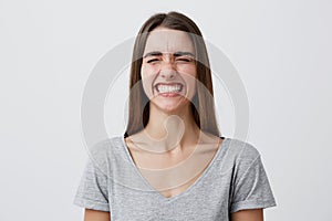 Young attractive cheerful caucasian student girl with dark long hair in casual gray t-shirt laughing brightly wit closed