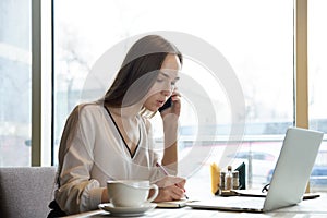 young attractive confident successful woman business woman talking on the phone and making notes in notebook sitting at a table i