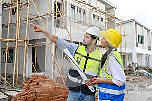 Young attractive construction man and woman in vests with helmets working on the under-construction building site. Home building