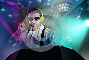 Young attractive and cool DJ in shirt and suspenders remixing music at night club using headphones in party strobo and flash